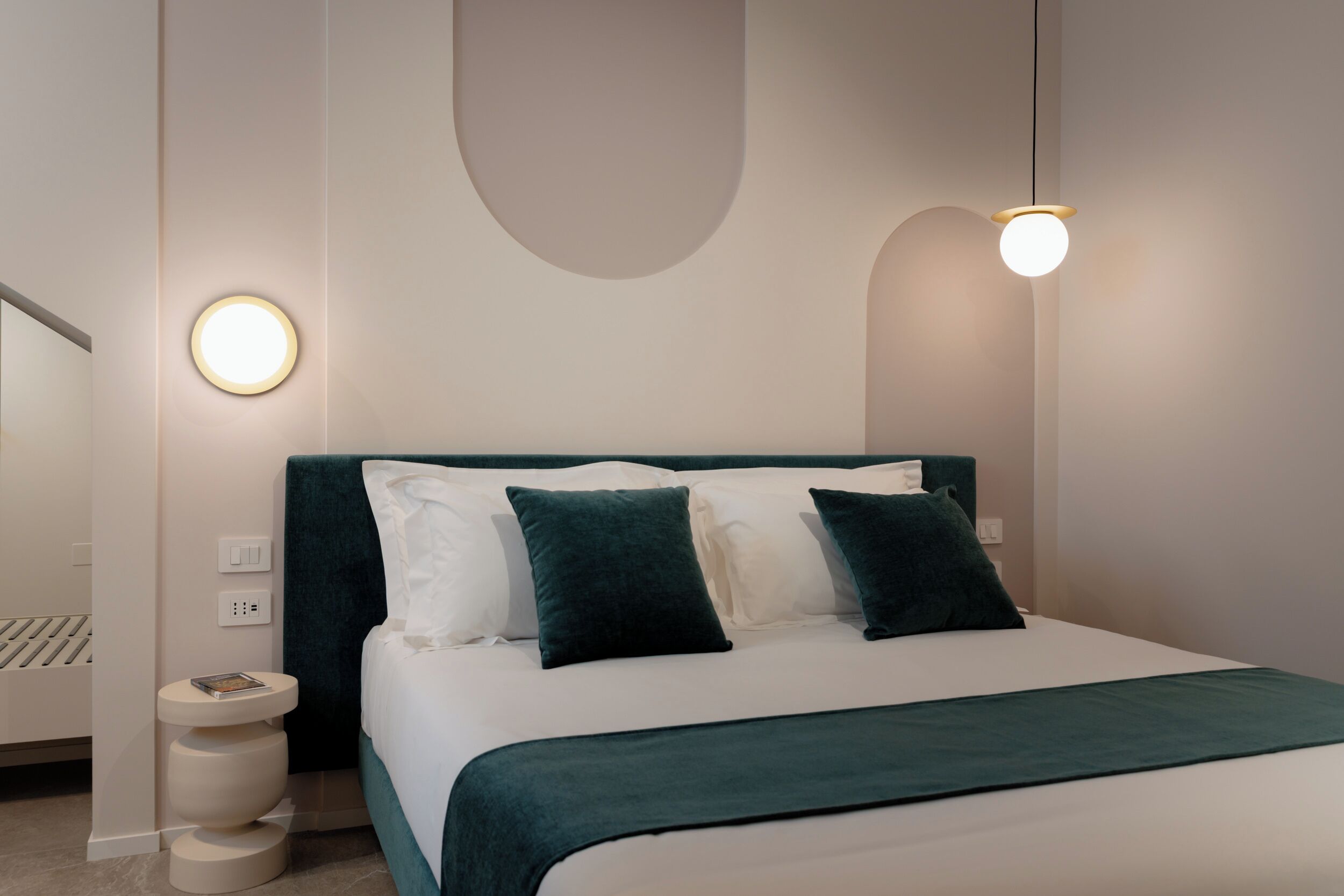 A modern bedroom with a bed, bedside tables, and a wall-mounted light fixture.
