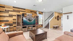 A modern living room with a wooden accent wall, a flat-screen TV, a coffee table, and a staircase leading to another level. - Happy Daze Home for 8 (Davenport)