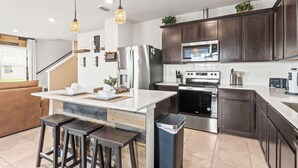 A modern kitchen with dark wood cabinets, stainless steel appliances, and a central island with stools. - Happy Daze Home for 8 (Davenport)