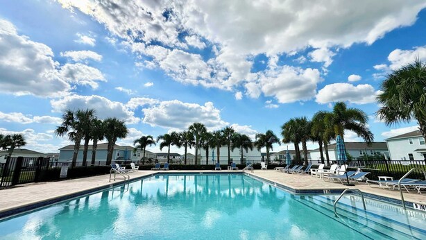 A swimming pool with lounge chairs and palm trees, surrounded by houses. - Happy Daze Home for 8 (Davenport)