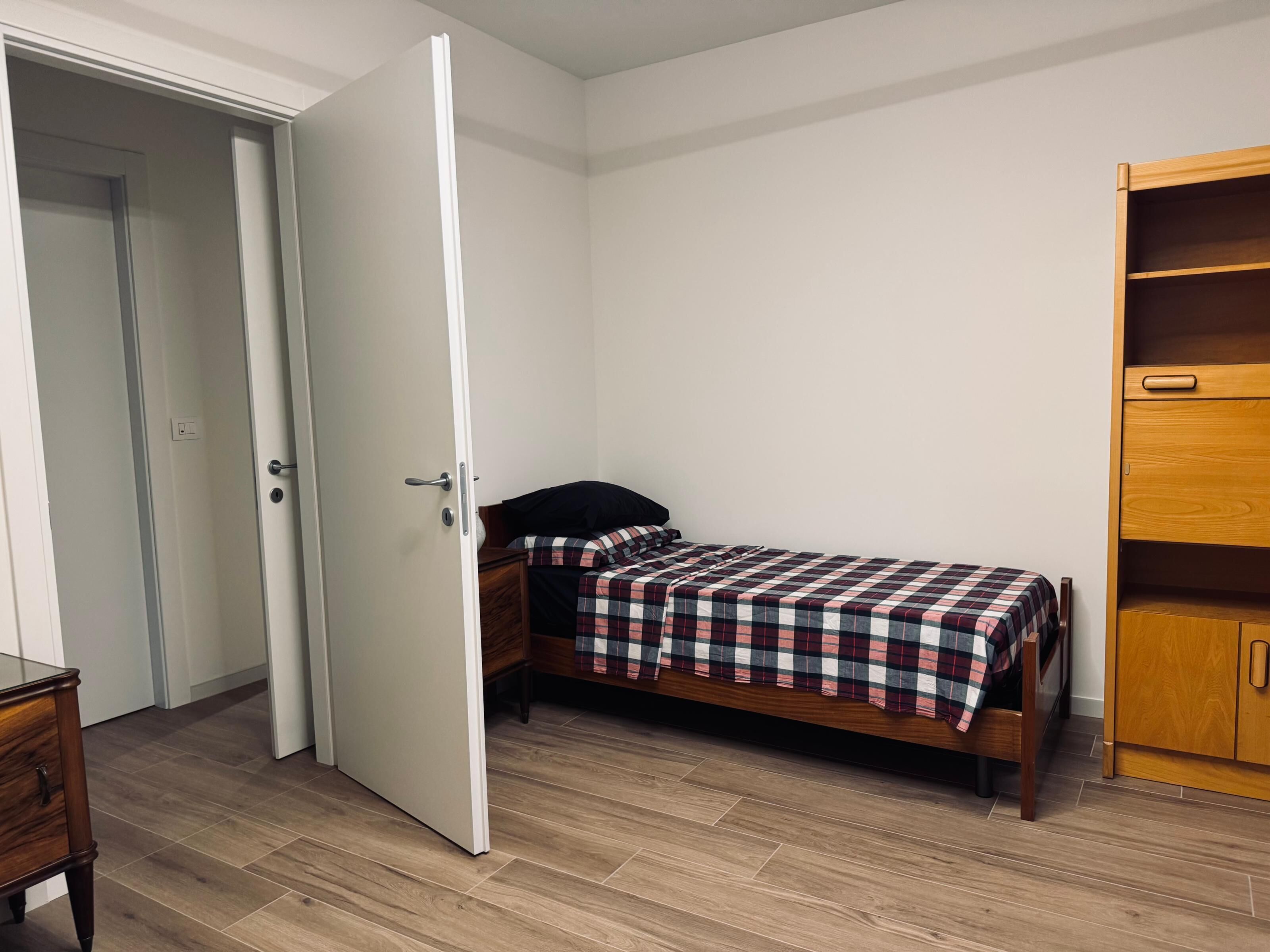 Une chambre à coucher avec un lit, une armoire en bois et une porte donnant sur une autre pièce.