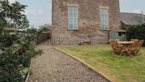 A stone building with two windows, a gravel path leading to a grassy area with a wooden table and chairs. - The Old Chapel (Berwick-upon-Tweed)