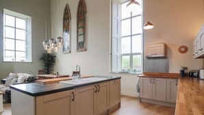 A spacious kitchen with a large island, wooden cabinets, and a dining area with a table and chairs. - The Old Chapel (Berwick-upon-Tweed)