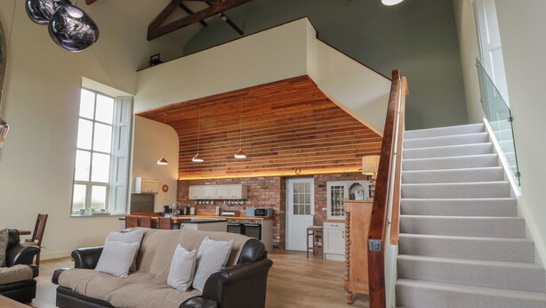 A spacious living area with a high ceiling, a fireplace, and a kitchen in the background. - The Old Chapel (Berwick-upon-Tweed)