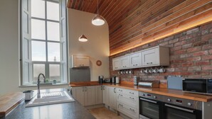 A modern kitchen with a large island, stainless steel appliances, and a brick wall backsplash. - The Old Chapel (Berwick-upon-Tweed)