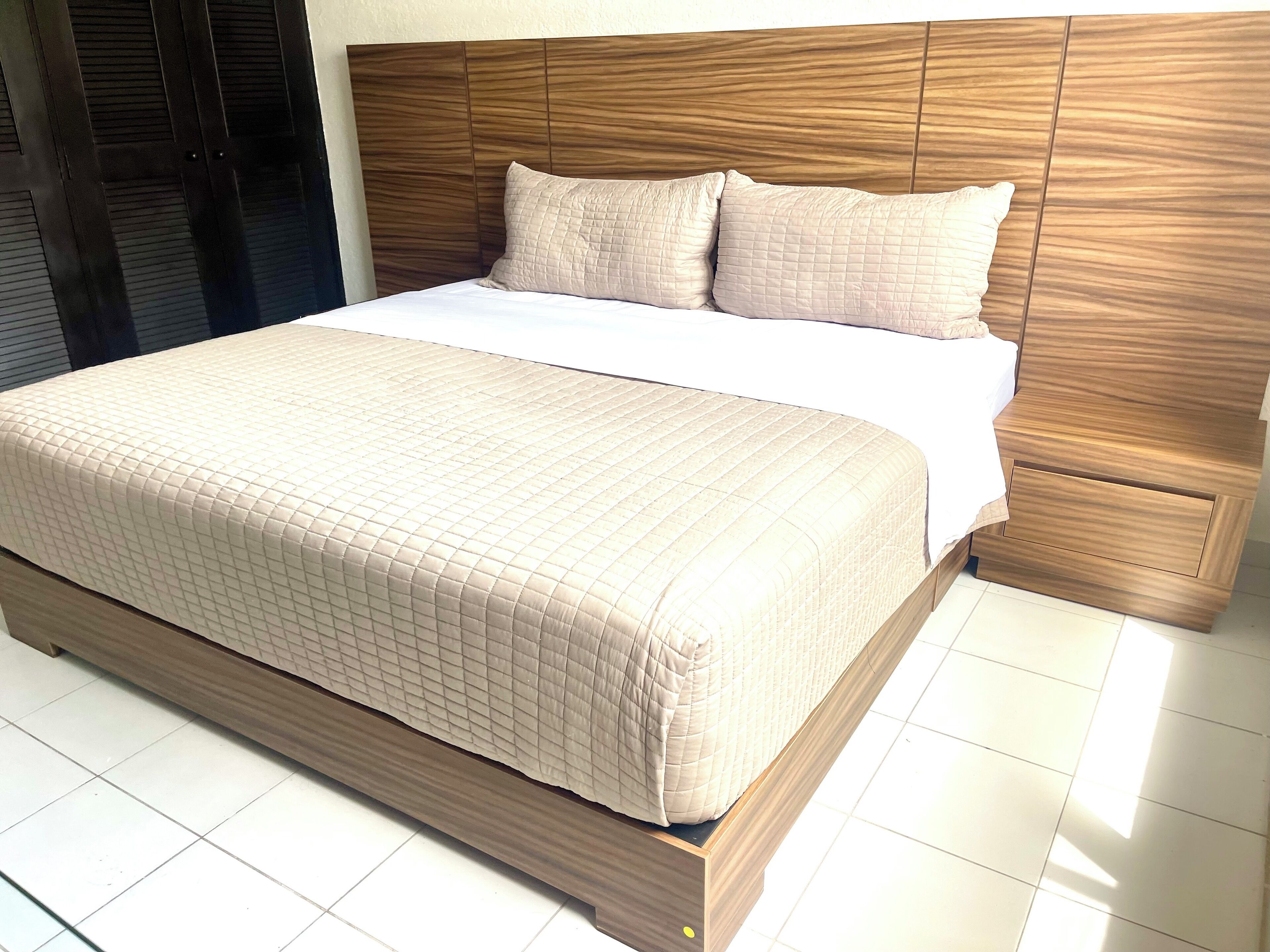 A large bed with a wooden headboard and a quilted beige bedspread.