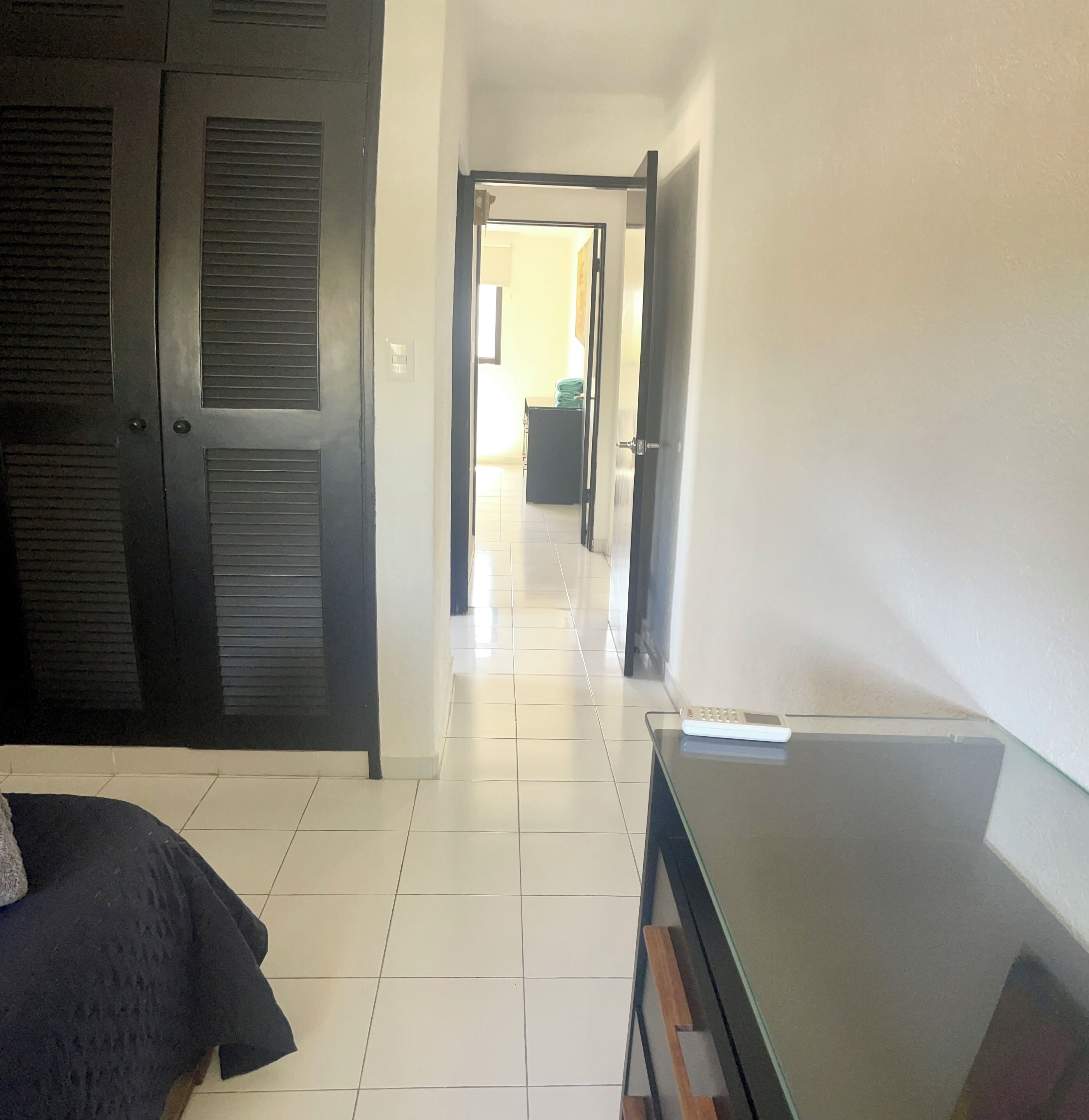 A hotel room with a bed, a desk, and a chair. There is a door leading to another room.