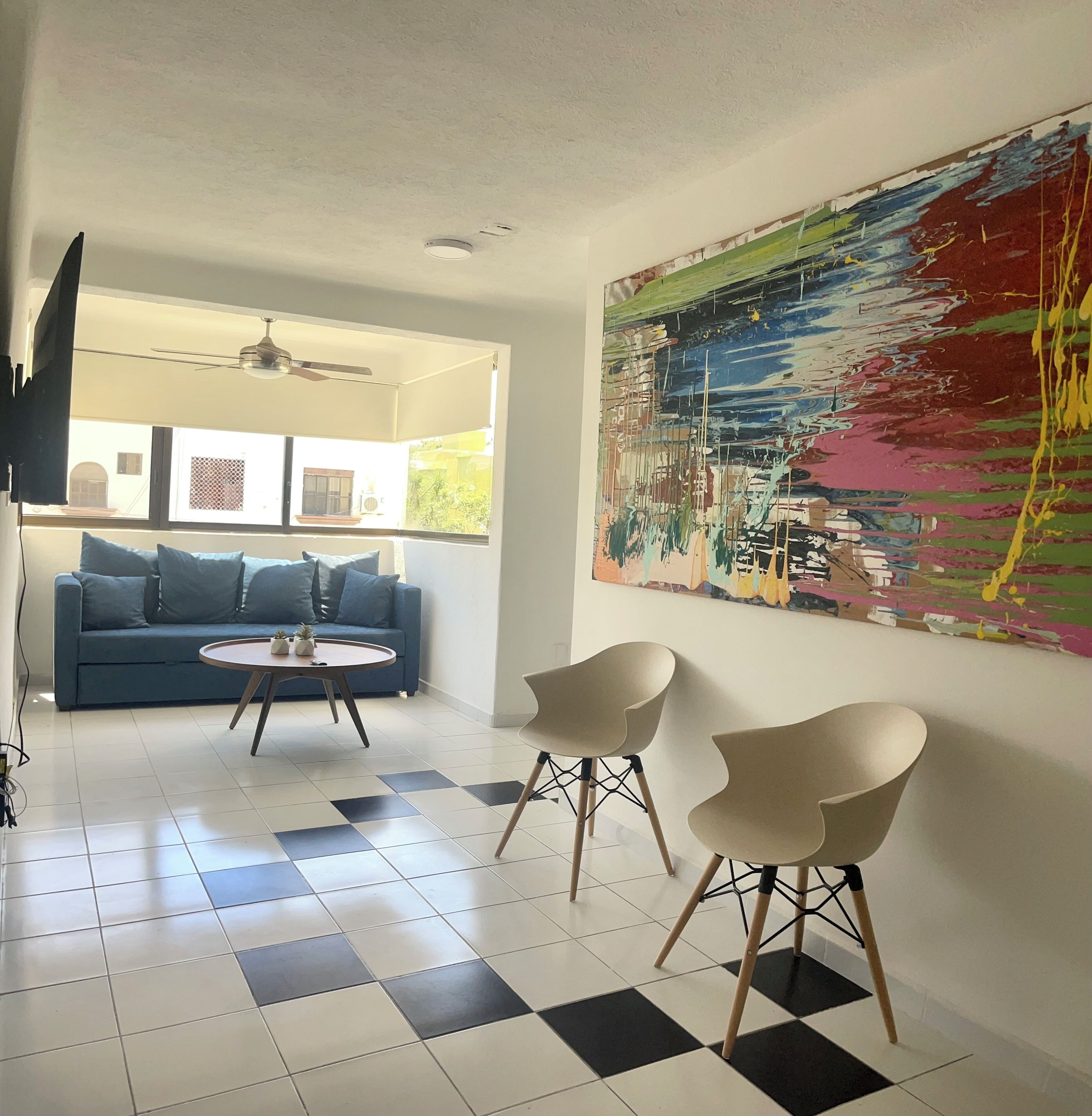 A modern living room with a blue sofa, two white chairs, a round coffee table, and a large abstract painting on the wall.