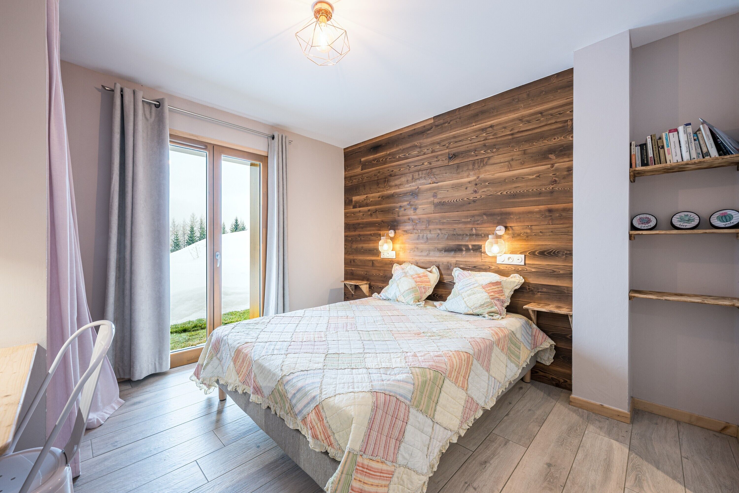 A bedroom with a wooden headboard, a bed with a quilt, a desk with a chair, and a bookshelf.