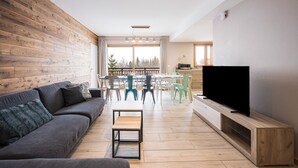 Una sala de estar moderna con un sofá, televisor, piso de madera y un comedor con sillas.