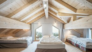 Ein Schlafzimmer mit geneigter Decke, zwei Betten, einem großen Fenster und Blick ins Freie.