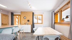 Ein Zimmer mit einem Holztisch, Stühlen, einer Küchenzeile und einem Fenster mit Blick auf eine verschneite Landschaft.