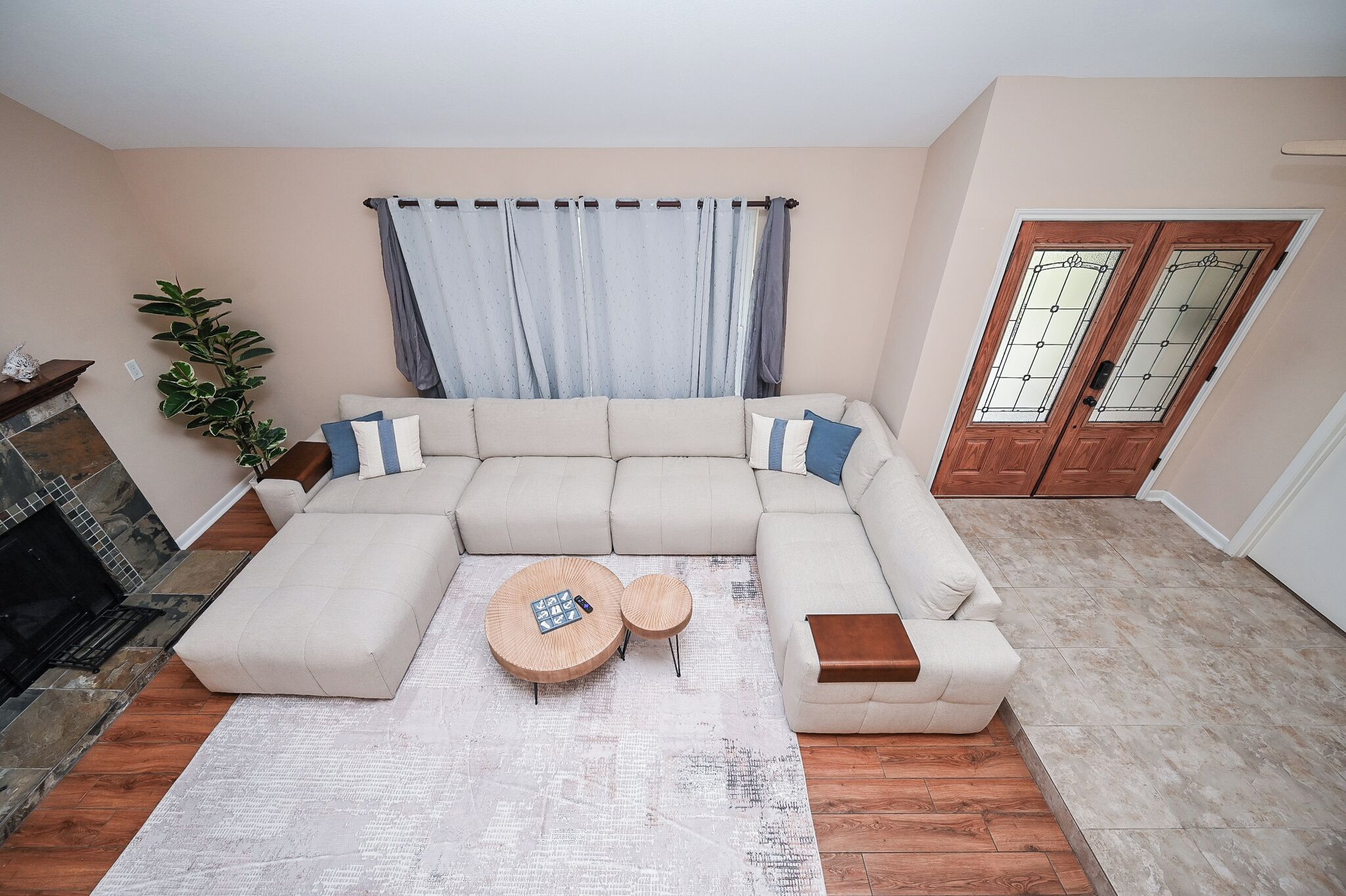 A living room with a sectional sofa, two round coffee tables, a potted plant, and a fireplace.