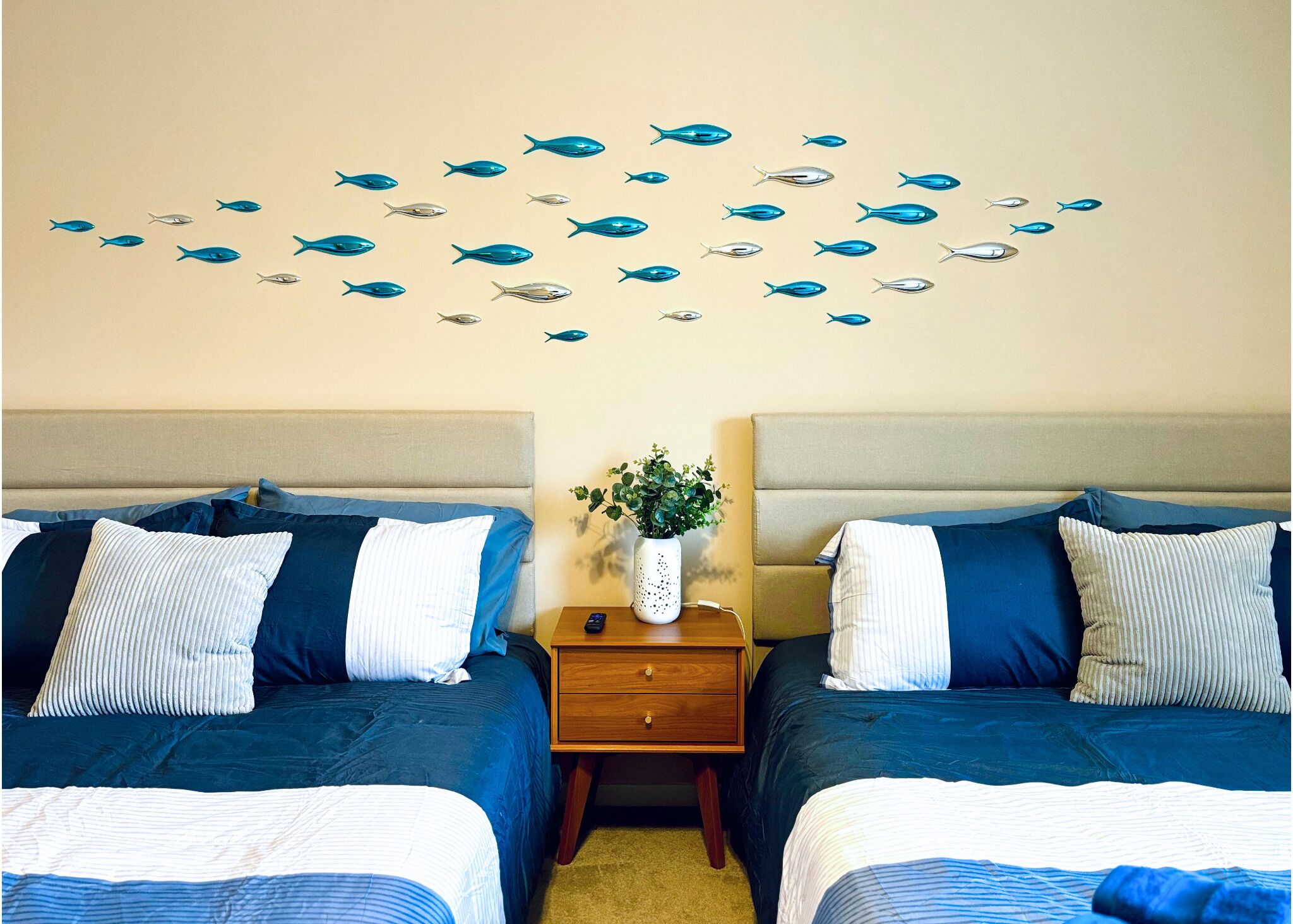 A hotel room with two beds, a nightstand, and a wall decoration of fish.