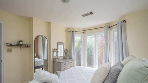 Ein Schlafzimmer mit Bett, Kommode, Spiegel und einem Fenster mit Vorhängen.