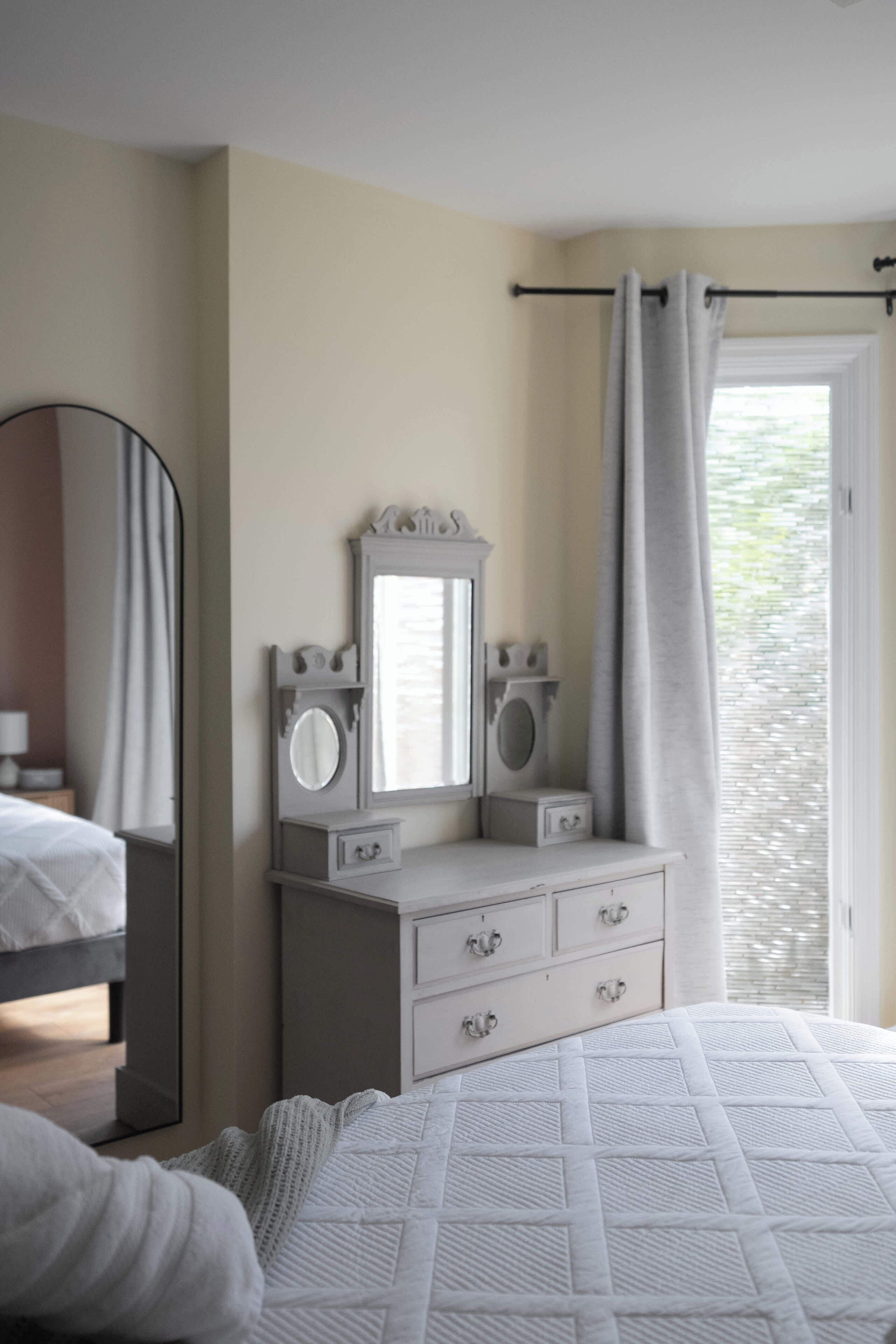 Un dormitorio con cama, cómoda, espejo y ventana con cortinas.