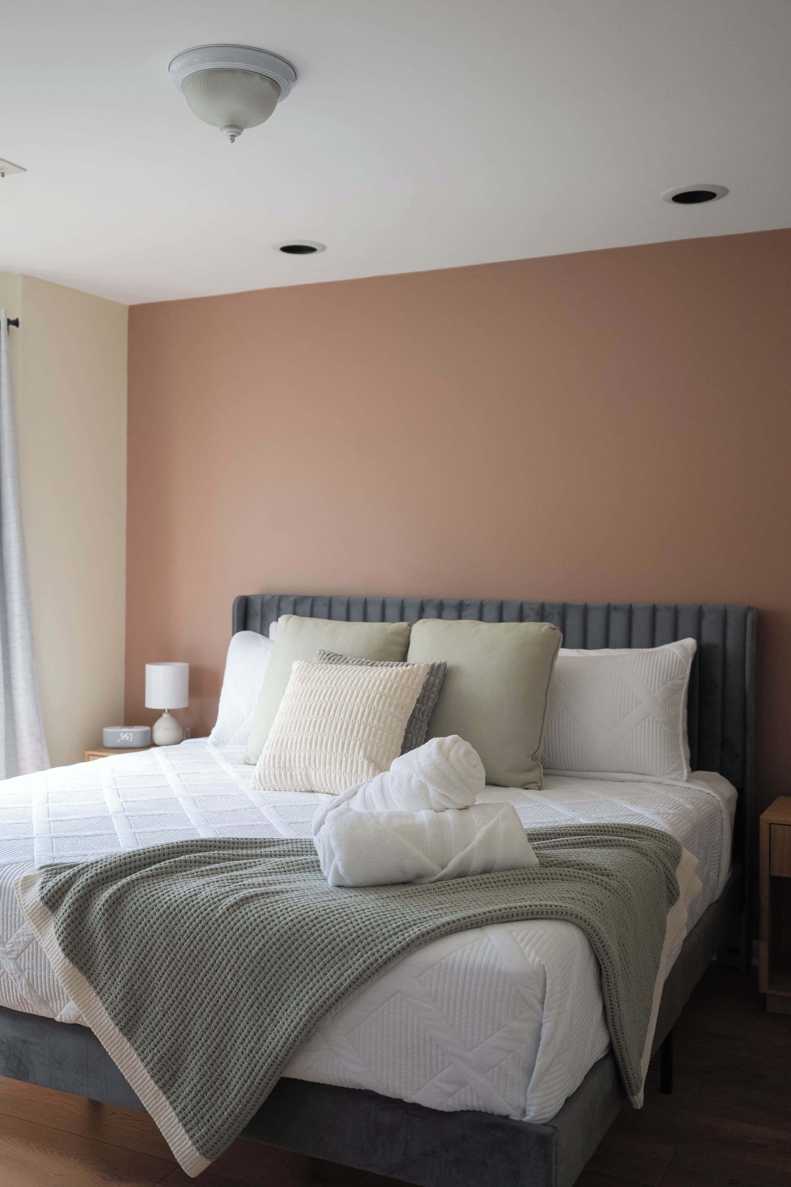 Una cama bien hecha con un cabecero gris, una lámpara de noche y un plaid verde.