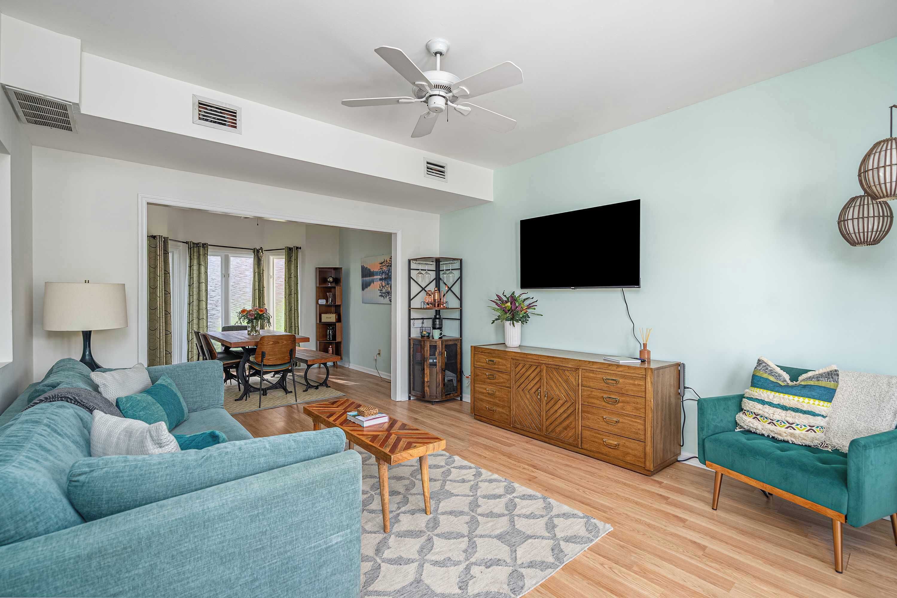 A spacious living room with a teal sofa, a wooden coffee table, and a TV mounted on the wall.