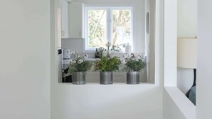 Ein heller, weißer Innenraum mit Fenster zum Garten, einer Küchenzeile mit modernen Geräten und einer Treppe, die in ein Obergeschoss führt.