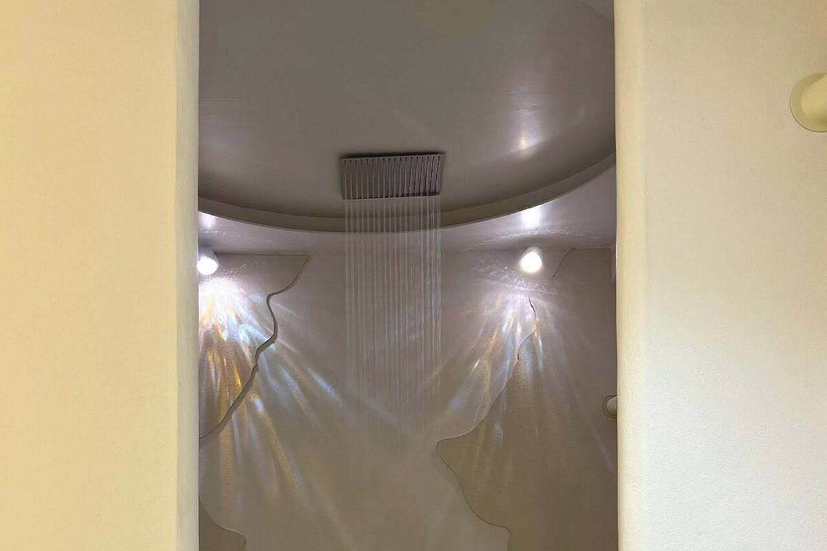 Een badkamer met een douche, betegelde vloer en een muur met een reliëfstructuur.