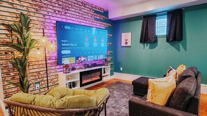 Una sala de estar con una televisión de pantalla plana, chimenea, pared verde y una silla de mimbre.