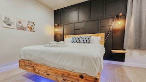Un dormitorio moderno con estructura de cama de madera, cabecera oscura e iluminación empotrada.