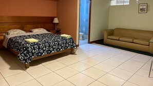 Ein Schlafzimmer mit einem Bett, einem Nachttisch, einer Lampe, einem Sofa und einem durch eine offene Tür einsehbaren Badezimmer.