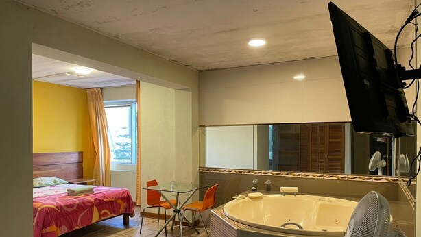 Ein Hotelzimmer mit Bett, einer Sitzecke mit Tisch und Stühlen, einer großen Badewanne, einem Spiegel und einem Fernseher.