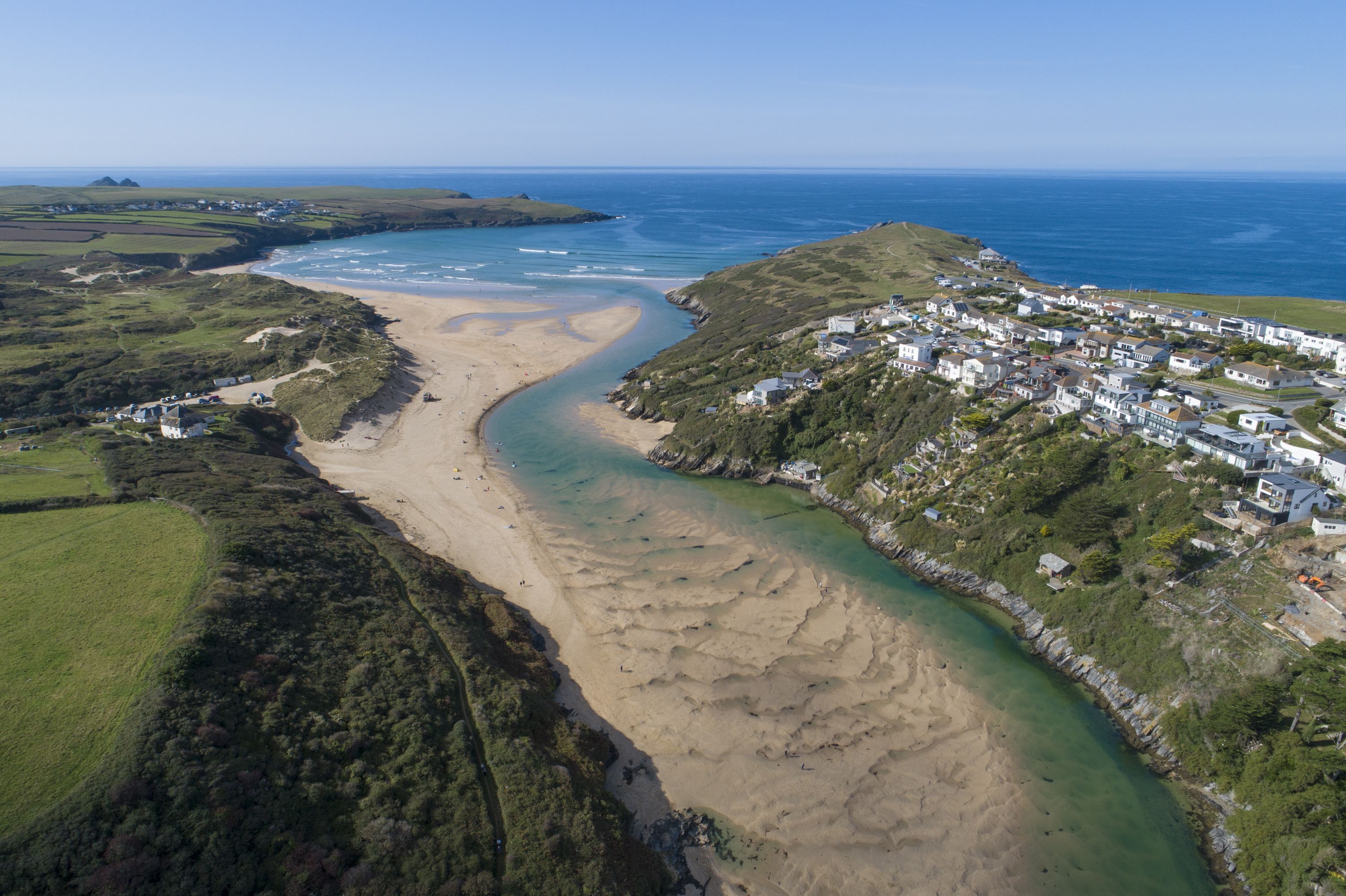 An aerial view of a coastal area with a beach, a small settlement, and a clear blue sky.