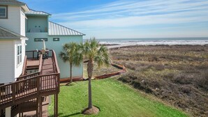 Una propiedad costera con una terraza frente a la playa, una palmera pequeña y vistas al océano.