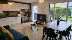 A modern kitchen with white cabinets, a dining area with a wooden table and chairs, and a TV displaying 'Family Garden'.