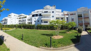 A modern multi-story residential building with balconies, a well-maintained lawn, and a clear blue sky.
