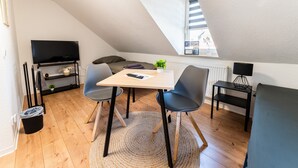 A loft-style room with a dining table, chairs, a TV, a sofa, and a small plant.