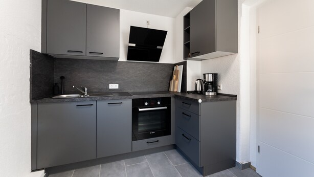 A modern kitchen with dark cabinetry, a built-in oven, and a coffee maker.
