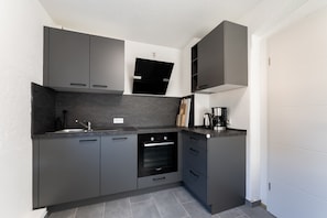 Uma cozinha moderna com armários escuros, forno embutido e cafeteira.