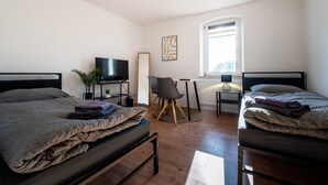 A bedroom with two beds, a desk, a chair, a TV, and a window.