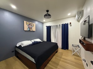 A modern bedroom with a bed, a ceiling fan, a TV, and a painting on the wall. - Barefoot (Bijagua de Upala)