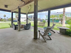 An outdoor patio area with concrete flooring, metal columns, wicker furniture, and a view of a residential neighborhood. - West Bay Getaway by Ryson Vacation Rentals (Galveston)