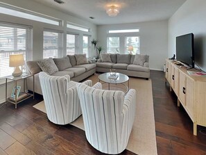 A modern living room with a sectional sofa, striped armchairs, a coffee table, and a TV on a wooden cabinet. - West Bay Getaway by Ryson Vacation Rentals (Galveston)