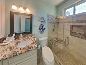 A bathroom with a glass-enclosed shower, a marble sink, a toilet, and a large mirror. - West Bay Getaway by Ryson Vacation Rentals (Galveston)