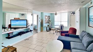 A living room with a television, a sofa, a coffee table, and a dining area with chairs and a table. - The Salty Fountain by Distinctive Beach Rentals (Daytona Beach)