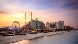 A coastal cityscape with a prominent Ferris wheel, high-rise hotels, and a beach. - The Salty Fountain by Distinctive Beach Rentals (Daytona Beach)