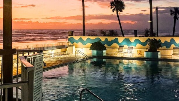 A pool area with lounge chairs and a view of the ocean at sunset. - The Salty Fountain by Distinctive Beach Rentals (Daytona Beach)