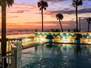 A pool area with lounge chairs and a view of the ocean at sunset. - The Salty Fountain by Distinctive Beach Rentals (Daytona Beach)