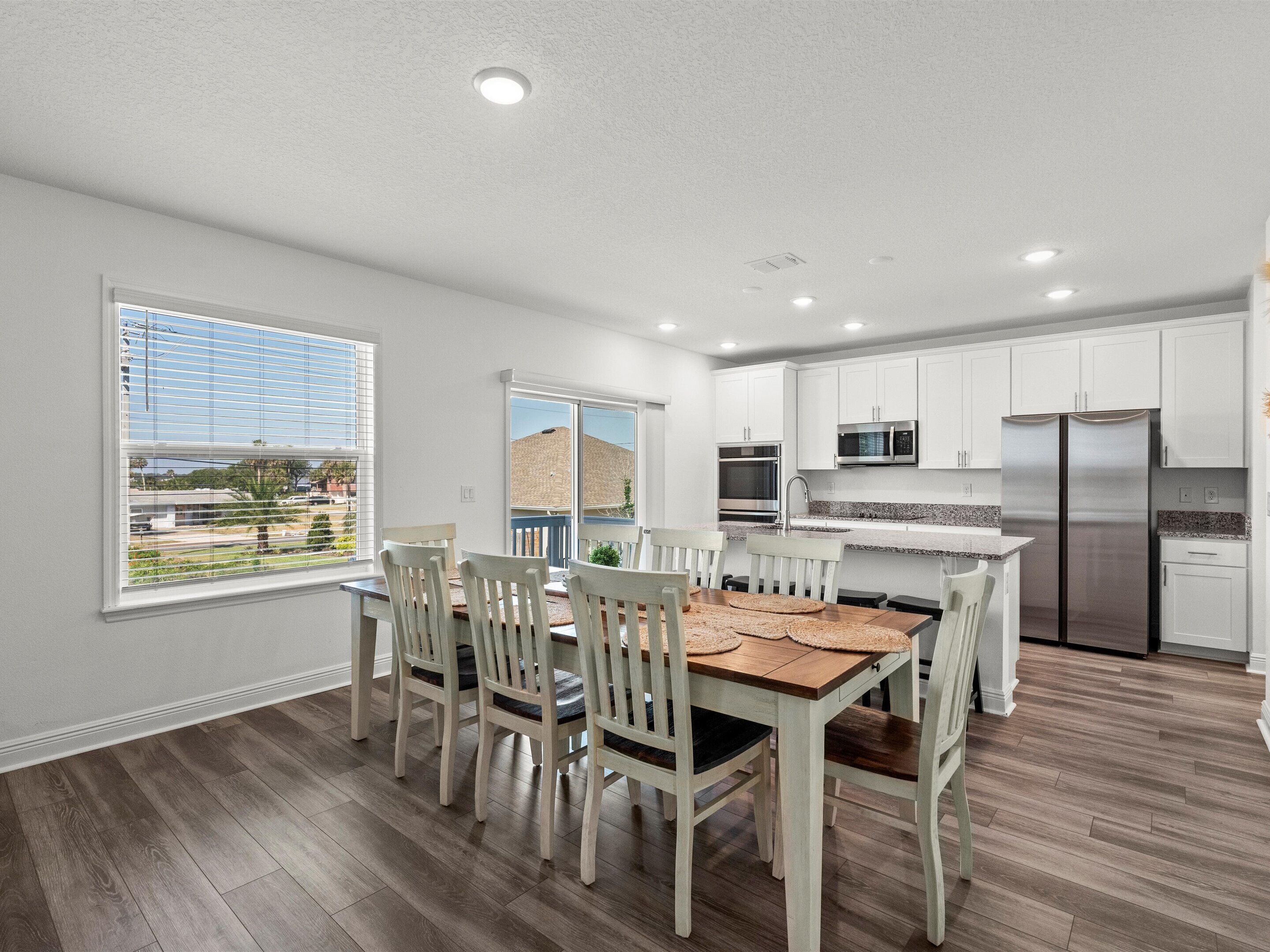 A modern kitchen with white cabinets, stainless steel appliances, and a dining area with wooden chairs and a table.