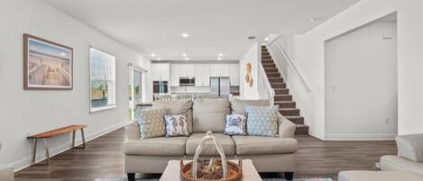 A modern living room with a beige sofa, a coffee table, and a staircase leading to another level.