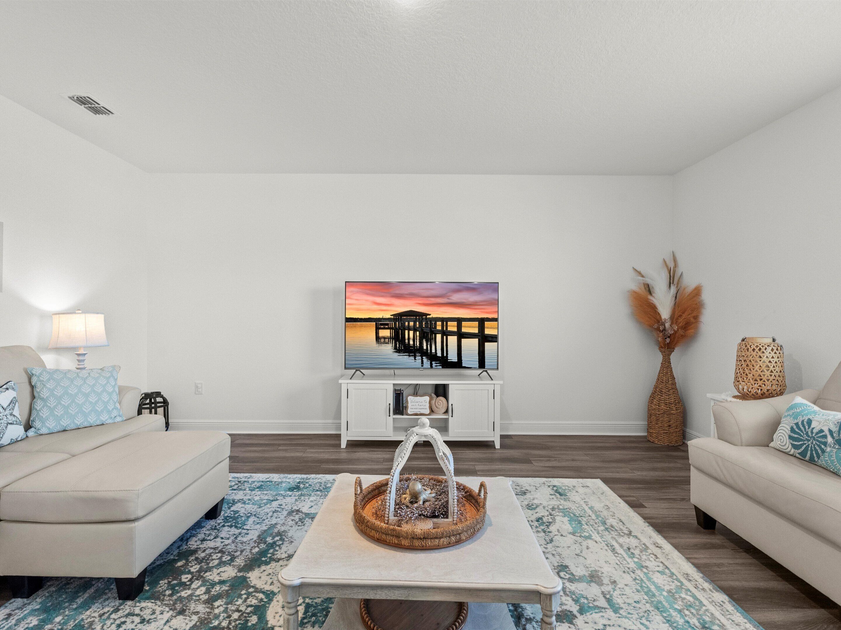 Un salon moderne avec un canapé blanc, une table basse et un tableau représentant un coucher de soleil sur une jetée.