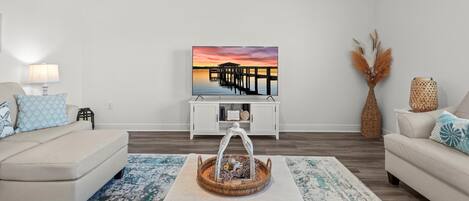 Un salon moderne avec un canapé blanc, une table basse et un tableau représentant un coucher de soleil sur une jetée.