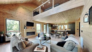 A spacious living area with a fireplace, a dining table, and a kitchen in the background.