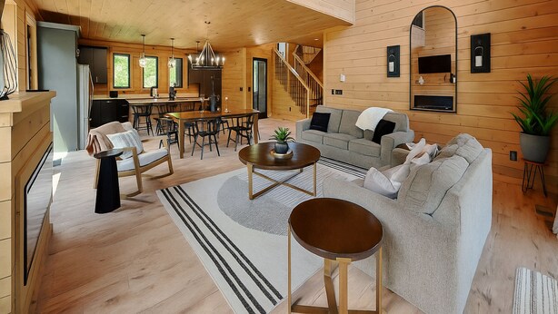 A spacious living area with a high ceiling, wooden walls, a dining area, and a staircase leading to an upper level.